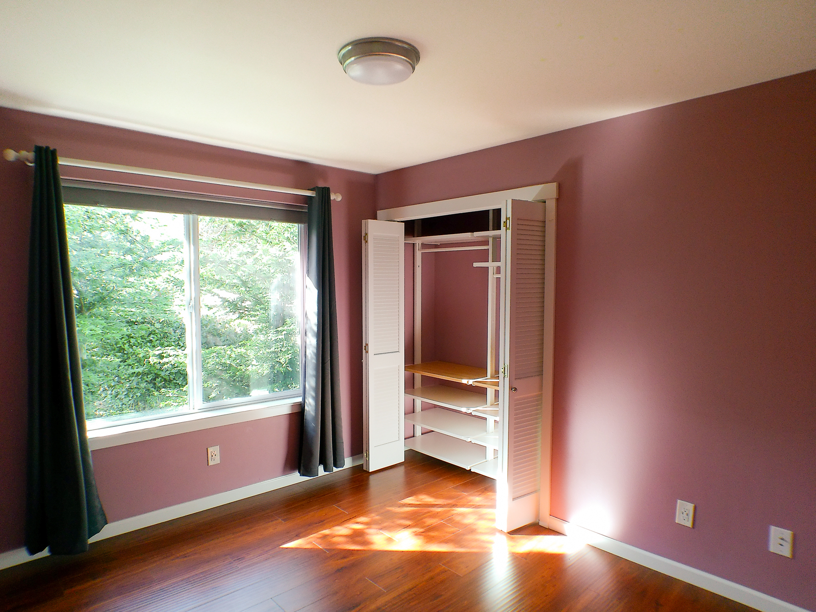 The second bedroom features large, bright windows complemented by a white ceiling that amplifies the natural light. Custom closets with louvered doors and window treatments complete the space.